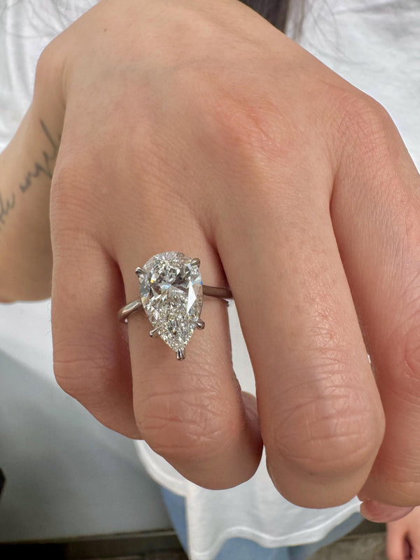 Pear-shaped diamond ring on a finger with a blurred background