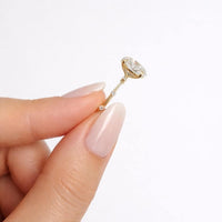 Gold earring with a large diamond held between fingers against a white background