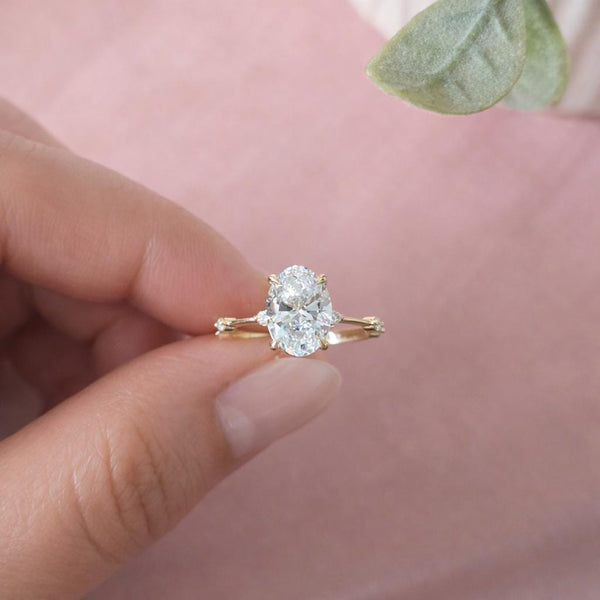 Gold ring with a heart-shaped diamond held by a hand against a soft pink background